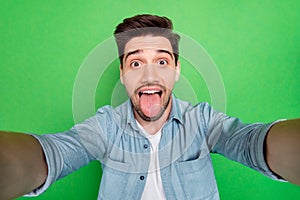 Closeup photo of handsome guy crazy playful mood making selfies sticking tongue out mouth wear denim shirt isolated