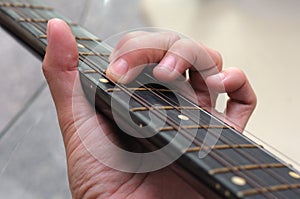 A closeup photo of the left hand fingers of a guitarist playing an acoustic guitar