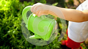 Closeup photo of little boy holding freen plastic watering can at garden