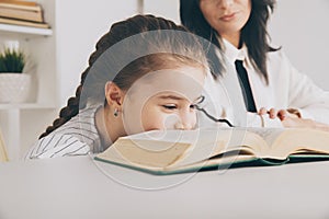 Closeup photo of little girl reading book and her mother behind.