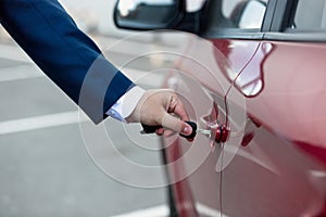 Closeup photo of man in suit opening car door with key