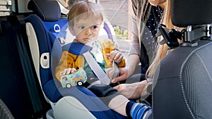 Closeup photo of mother fastening belts on her son car safety seat