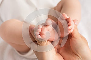 Closeup photo of mother`s hands holding baby`s tiny feet on  white cloth background