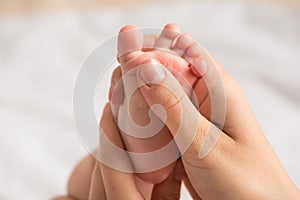 Closeup photo of mother`s hands massaging baby`s tiny foot on isolated white background