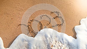 Closeup photo of ocean waves rolling over 2023 numbers written on wet sand. Concept of New Year, Christmas and travel on