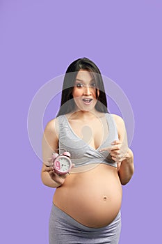 Closeup photo of pregnant woman in underwear holding red alarm clock at tummy