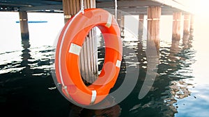 Closeup photo of red saving ring hanging wooden pier. Safety on sea water