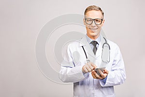 Closeup photo of senior man doctor standing isolated on grey background, using mobile phone