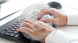 Closeup photo of slim female hands typing text on computer keyboard