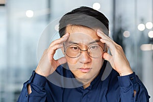 Closeup photo of thinking sad asian businessman, man in glasses looking at camera disappointed, boss in shirt inside