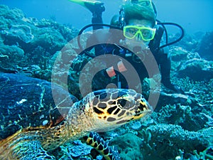 Closeup photo of a turtle and a young women scuba diver. The diver is looking forward. The turtle is on foreground.