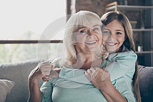 Closeup photo of two best friends people cute aged granny small grandchild girl sit comfortable sofa hug piggyback