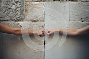 Closeup photo of two hands holding each other in front of stone wall. Concept of Israeli-Palestinian conflict