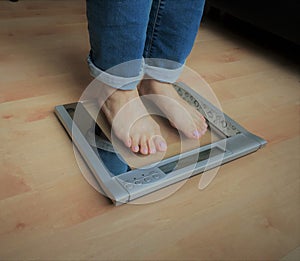 Closeup photo of woman feet standing on weight sacle over the hardwood floor