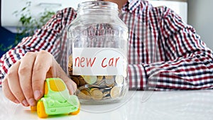 Closeup photo of young man buying new car. Jar full of money and miniature toy car on white table