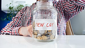 Closeup image of young man with glass jar full of money for buying new car