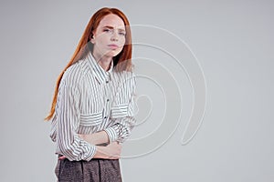 Closeup photo of young sad redhead businesswoman in striped shirt holding her stomach indigestion studio white photo