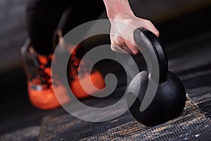 Closeup photo of young woman in the black leggings and orange sneackers while push-ups with kettlebell.