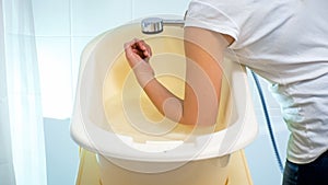 Closeup photo of young woman checking water temperature in baby bathtub with elbow