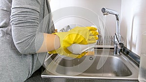 Closeup photo of young woman in rubber gloves washing dishes