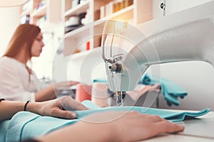 Closeup photo of young woman`s hands seamstress sitting and sews on sewing machine in creative designer studio