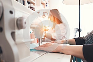 Closeup photo of young woman`s hands seamstress sitting and sews on sewing machine in creative designer studio