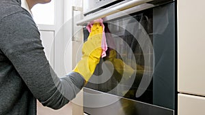 Closeup photo of young woman with in yellow gloves washing dirty stained glass oven door