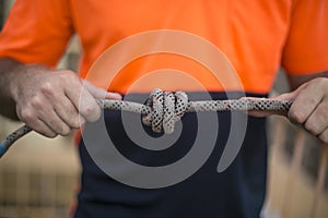 Closeup pic of male rope access industrial worker, inspecting tying a knot into static twin ropes before working and abseiling