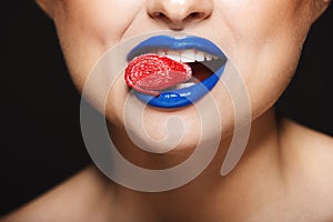 Closeup picture of cheerful girl`s colorful lips holding sweeties with teeth.