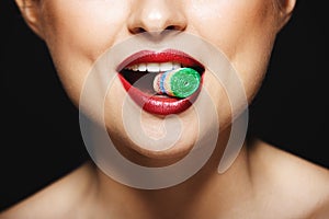 Closeup picture of cheerful girl`s lips holding sweeties with teeth.