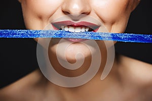 Closeup picture of cheerful girl`s lips holding sweeties with teeth.
