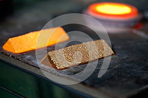 Closeup picture of ingots of melt gold, hot shiny metal bars on table and fire furnace on background