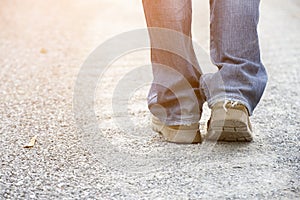 Closeup picture of legs of traveler walking on small pathway.Foot of Lonely man or woman wearing old blue jeans and fashion brown