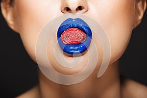 Closeup picture of woman`s colorful lips holding sweeties.