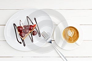 Closeup piece of homemade cake with cherries and cup of coffee cappuccino on white wooden table.