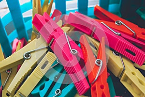 Closeup of a pile of colorful clothes pegs in a blue plastic bucket with holes