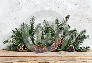 Closeup of pine leaves and cones on a wooden surface, against a white wall. Christmas background