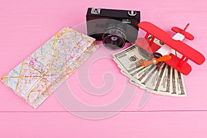 Closeup on a pink background camera, plane, map and money.