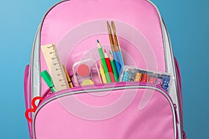 Closeup of pink backpack with office supplies against a blue background. Back to school. The concept of education