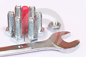 Closeup of pink bolt n a group of galvanized metallic screws, wrench and nut. Dissimilarity, uniqueness, originality concept