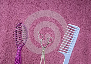 Closeup of pink brush,blue comb,scissors against hairy background.Empty space