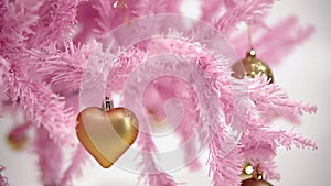 Closeup of pink colored artificial Christmas tree decorated by golden toys in shape of heart