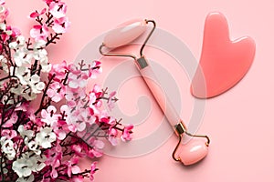 Closeup of pink jade roller, jade gua sha massager stone and almond blossoms. Skin care products concept