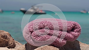 Closeup pink soft pink towel Mediterranean sea shore with blue lagoon at background. Clean textile laundry advertisement