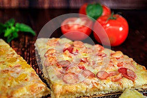 Closeup pizza slice with sausage, ham and cheese on brown wooden background