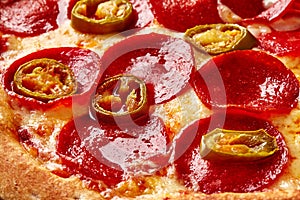 Closeup of pizza with slices of pepperoni and jalapenos on melted cheese with tomato sauce