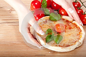 Closeup of pizza with tomatoes, cheese, basi and woman's handsl on wooden background