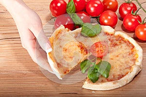 Closeup of pizza with tomatoes, cheese, basi and woman's handsl on wooden background