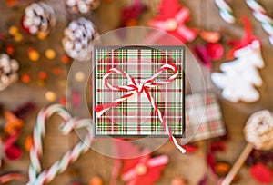 Closeup of plaid gift box with striped twine bow, Christmas decor in soft focus on wooden surface below