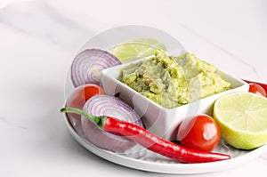 Closeup of plate with different ingredients,vegetables and bowl with fresh tasty guacamole on white table